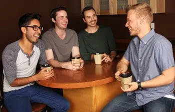 Four men sitting around a table with coffee cups, talking