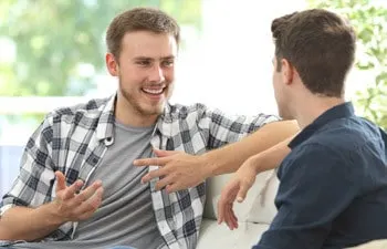 Two men sitting on a sofa in conversation, one gesturing as he speaks