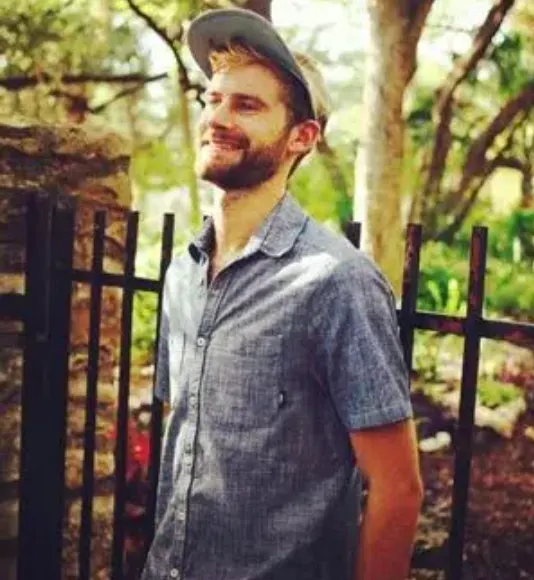 Man smiling outdoors near an iron fence, symbolizing freedom, transformation, and hope after breaking free from the downward spiral of addiction.