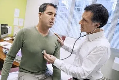 A doctor listening to a seated man’s chest with a stethoscope during a medical assessment