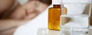 A close-up of sleep aid pills with a glass of water and a person sleeping in the background.