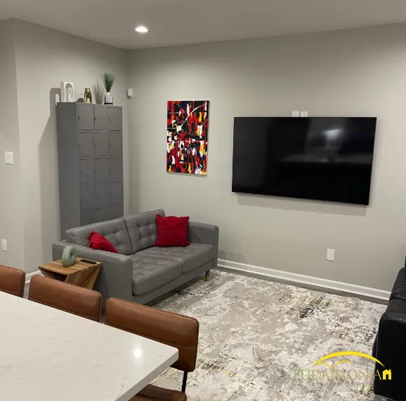 A community lounge with a sofa, lockers, a large television and artwork in a Houston sober living home