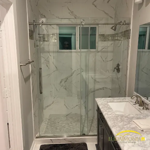An updated bathroom with a glass walk-in shower and marble tile in a Houston sober living home